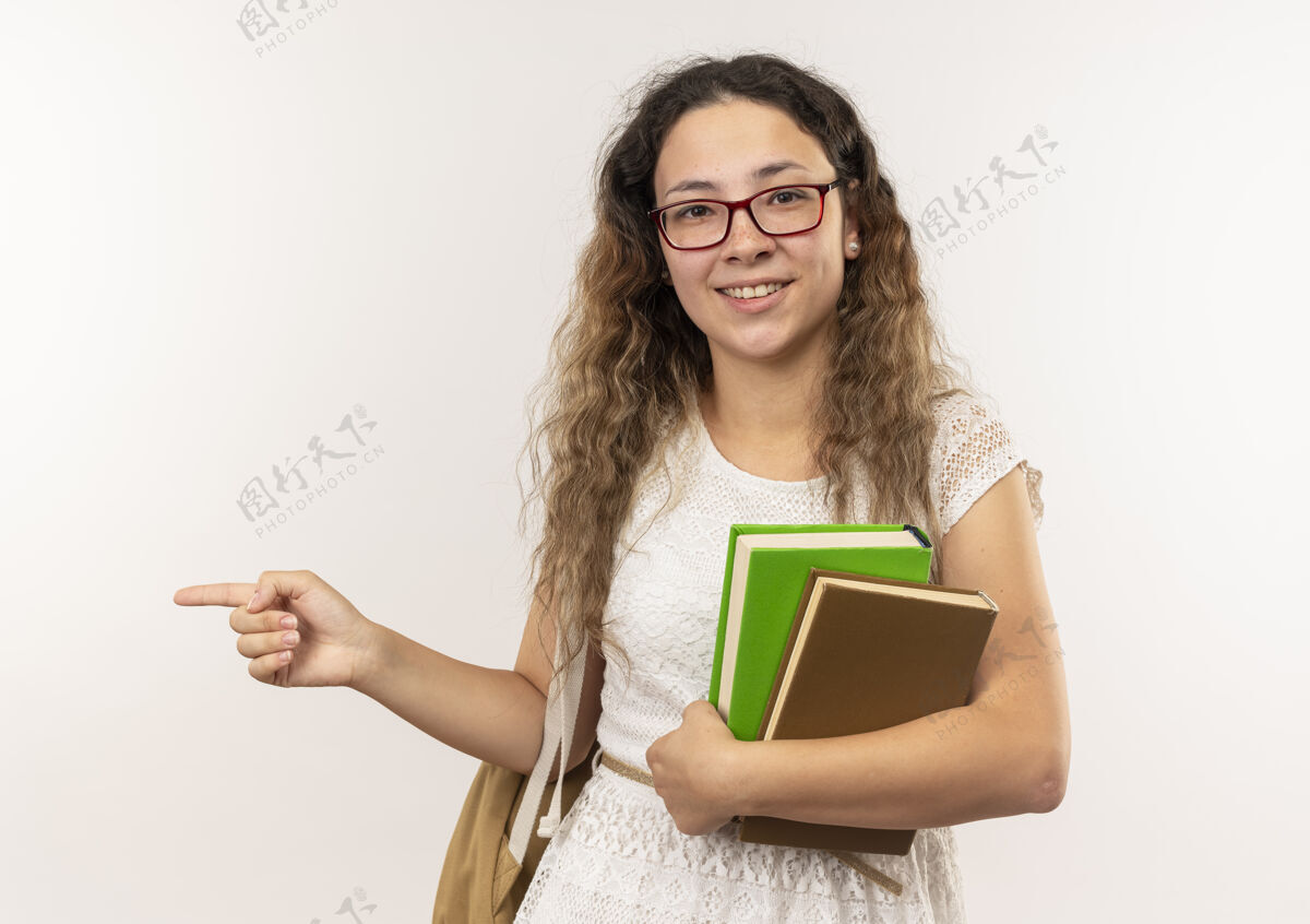 人面带微笑的年轻漂亮的女学生戴着眼镜 背着书包 指着隔离在白色墙上的一侧表情姿势感觉
