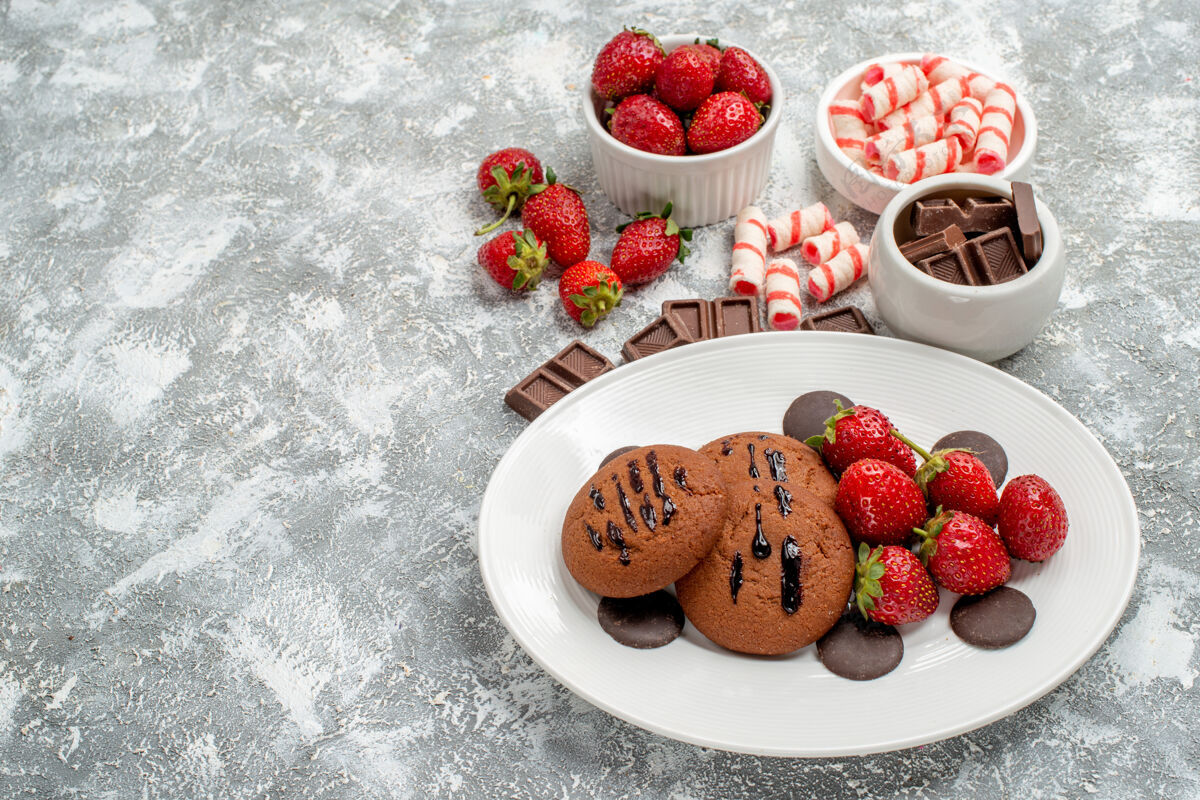 碗在白色盘子上的底视图饼干草莓和圆形巧克力 在灰白色地面上的碗糖果草莓巧克力巧克力水果食品