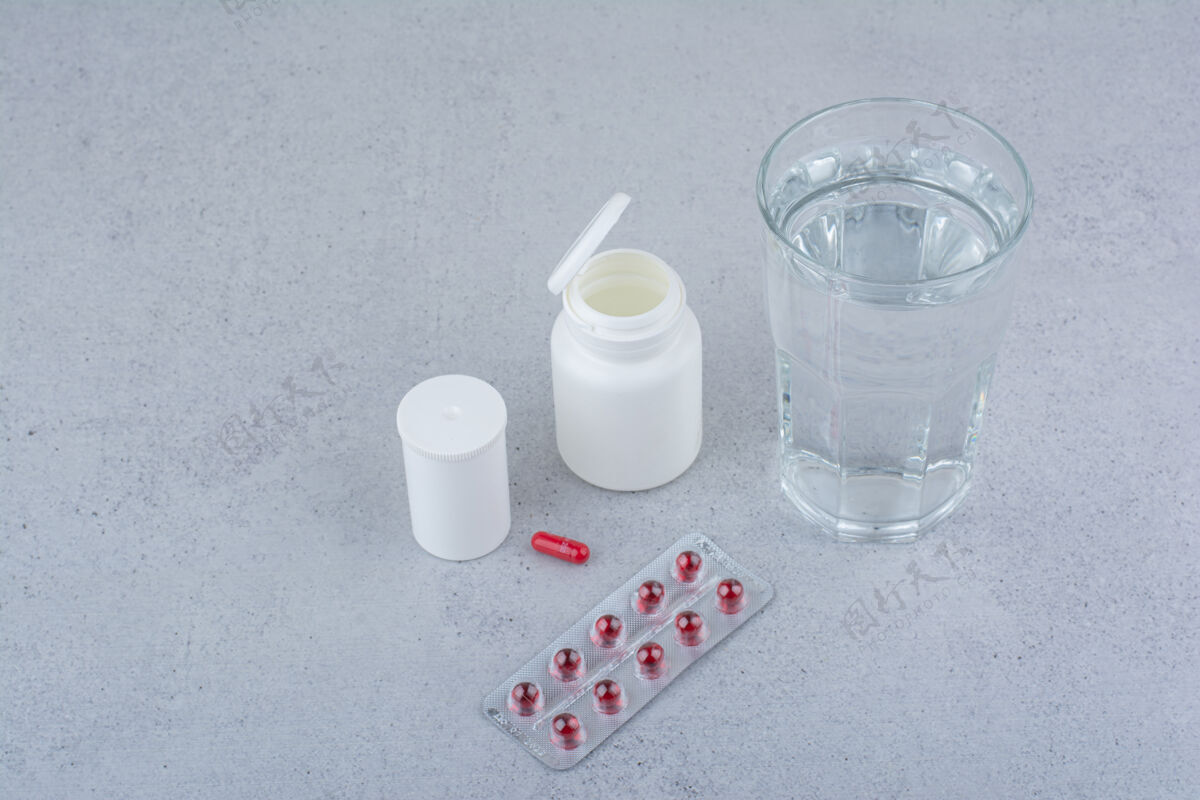 水红色的药丸 容器和大理石表面的一杯水抗生素药品片剂