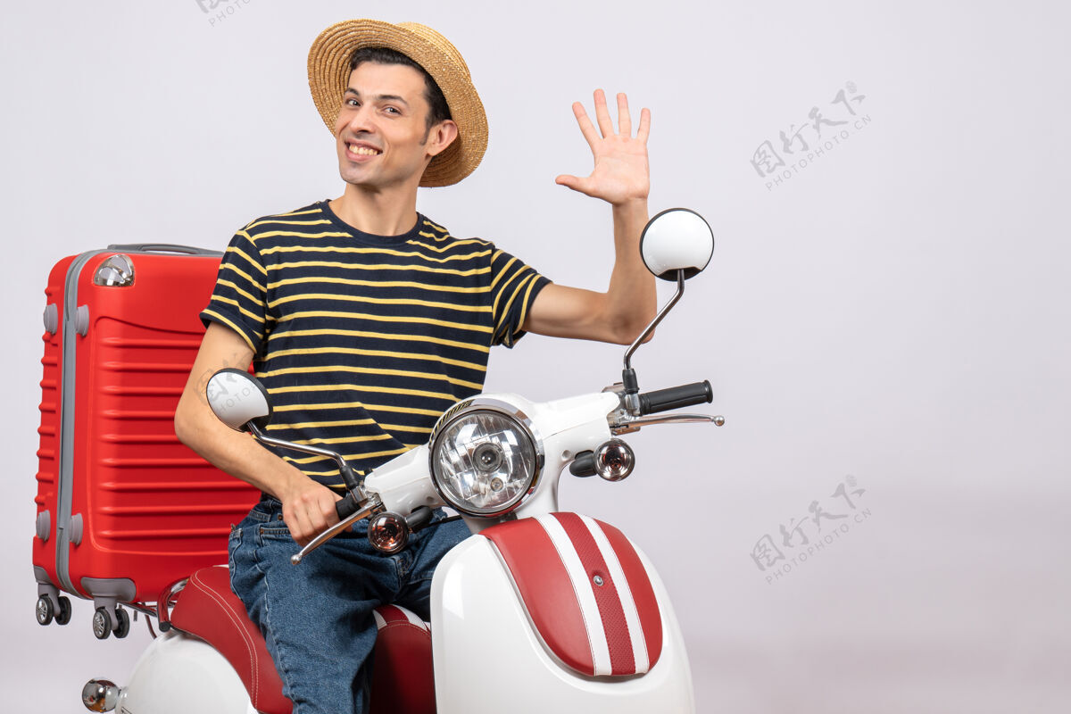 摩托车帅气的年轻人戴着草帽坐在轻便摩托车上挥舞着手的正面图车辆微笑帽子