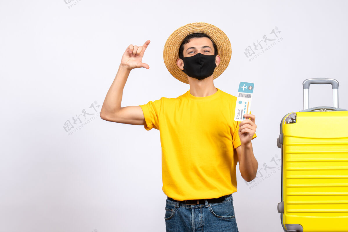 手指正面图穿着黄色t恤的年轻人站在黄色手提箱旁 举着旅行票 用手指显示大小男性头饰黄色