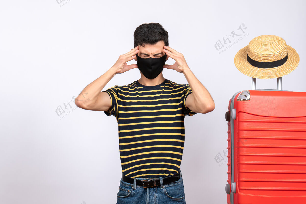 休闲正面图疲惫的年轻游客戴着黑色面具站在红色手提箱旁视图人姿势