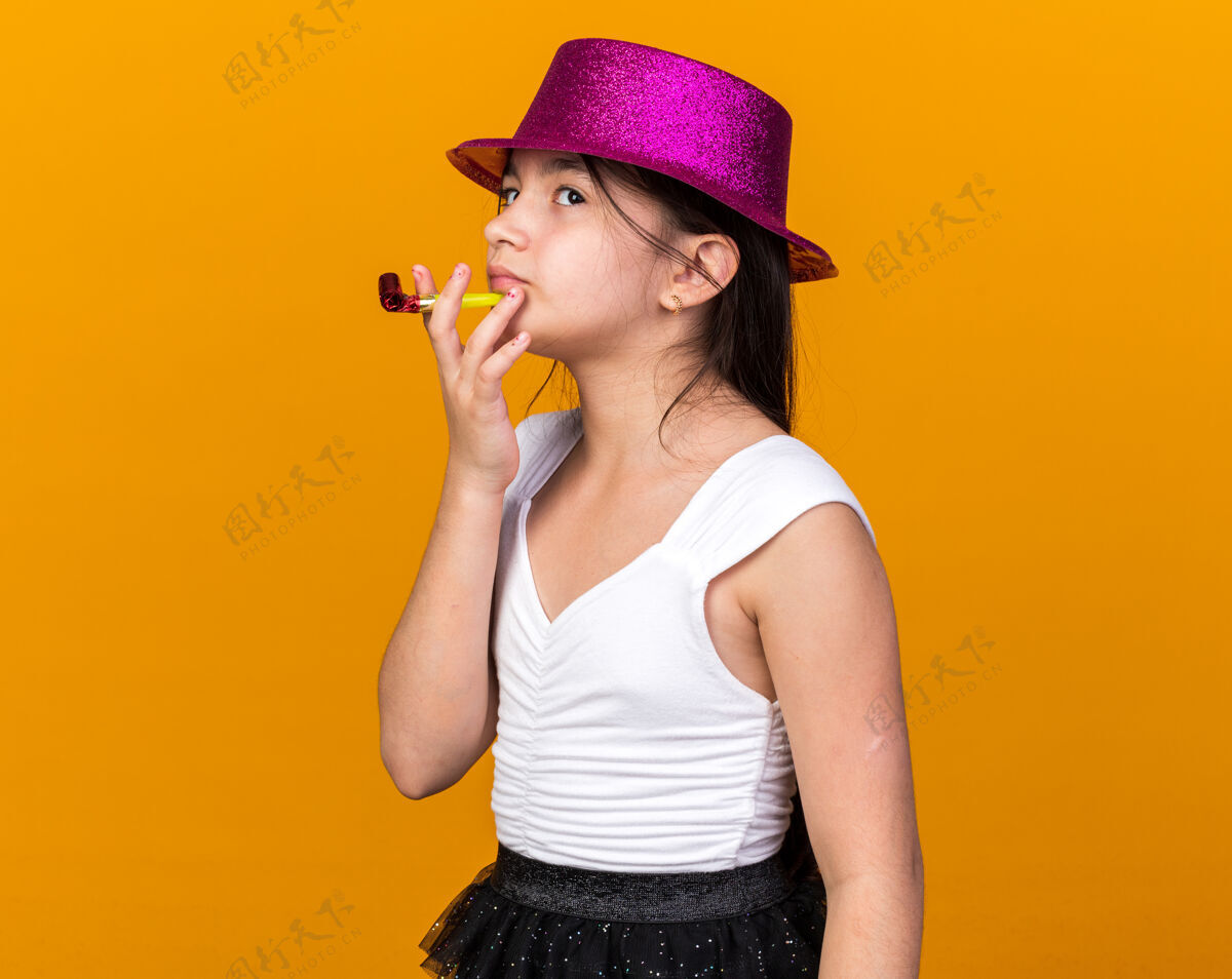 年轻体贴的年轻白人女孩 戴着紫色的派对帽 抬起头 手持派对哨子 孤立地站在橙色的墙上 留着复制空间手持女孩哨子