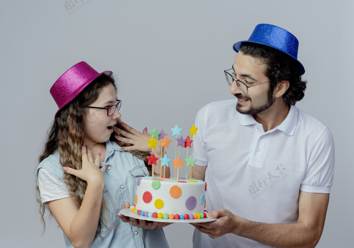 帽子快乐的年轻夫妇戴着粉色和蓝色的帽子男孩给女孩生日蛋糕粉色白色男孩