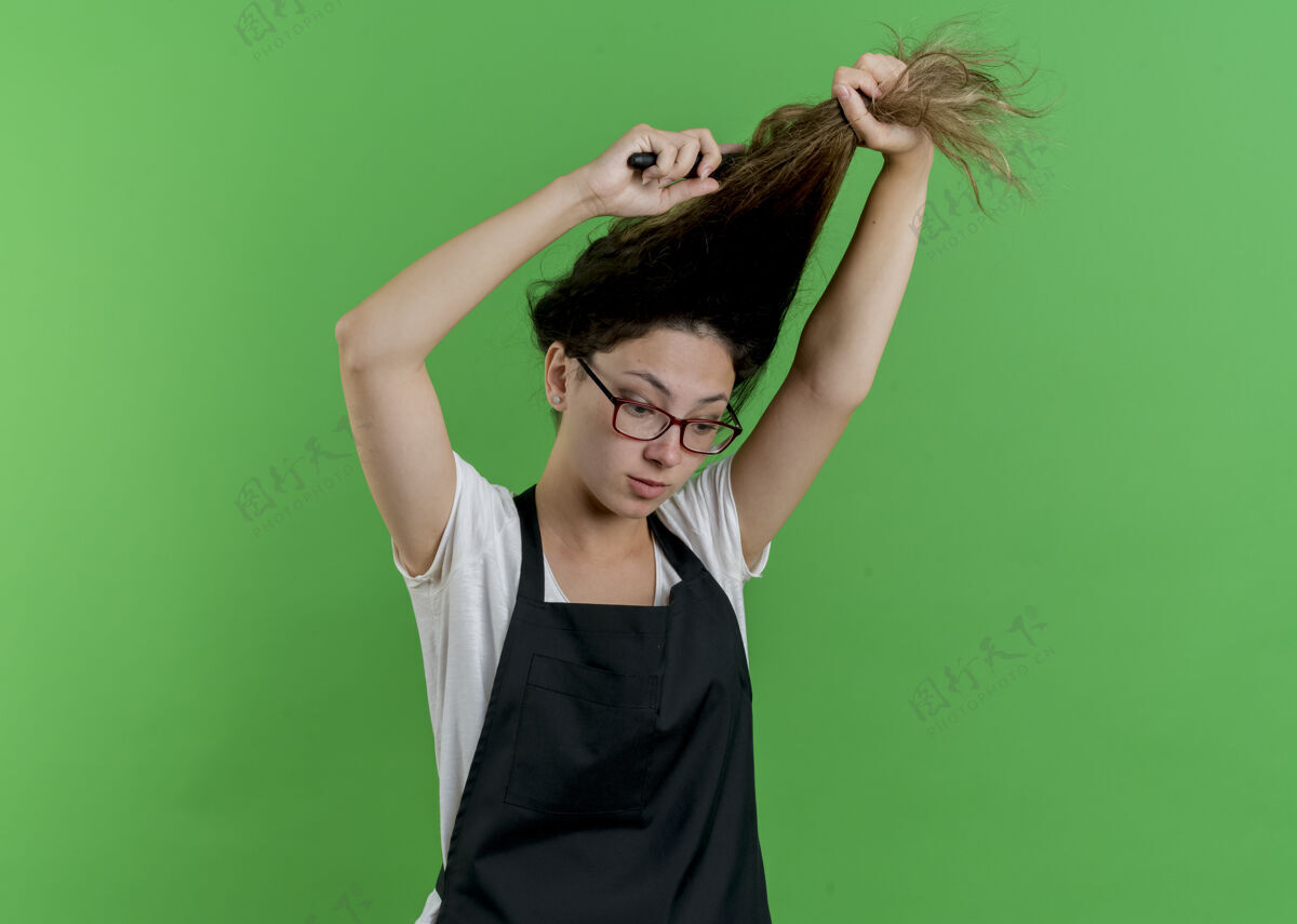 脸年轻的专业美发师站在绿色的墙上 围着围裙刷洗头发理发师表情人