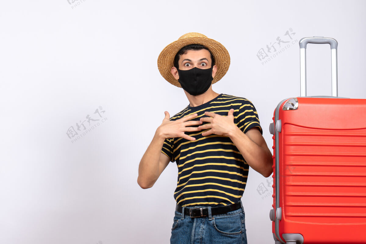 人正面图：戴着黑色面具的年轻游客睁大眼睛站在红色手提箱旁指着自己年轻的游客指着帽子