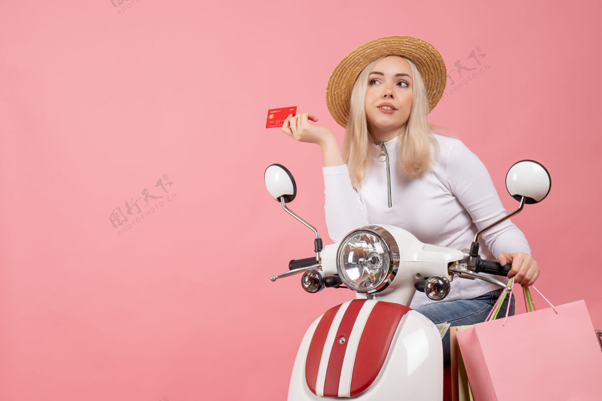 前排前视图骑着轻便摩托车的年轻女士拿着卡片在想什么小姐思考坐着
