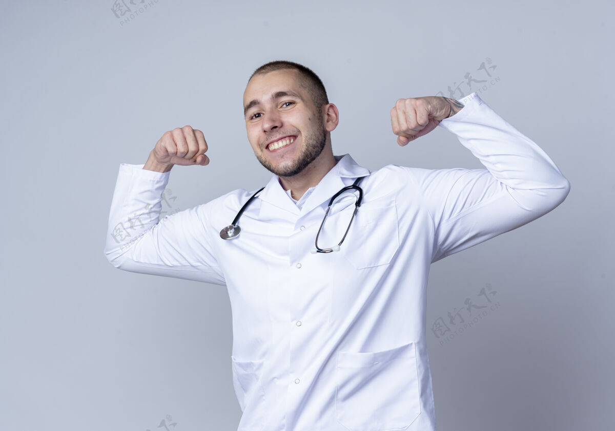 公民面带微笑的年轻男医生 穿着医用长袍 脖子上戴着听诊器 在白色的墙上做着强烈的孤立的手势人听诊器微笑
