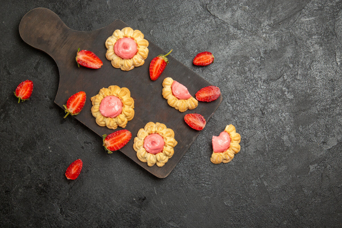 食品灰色表面上草莓奶油小甜饼的俯视图草莓花瓣珠宝