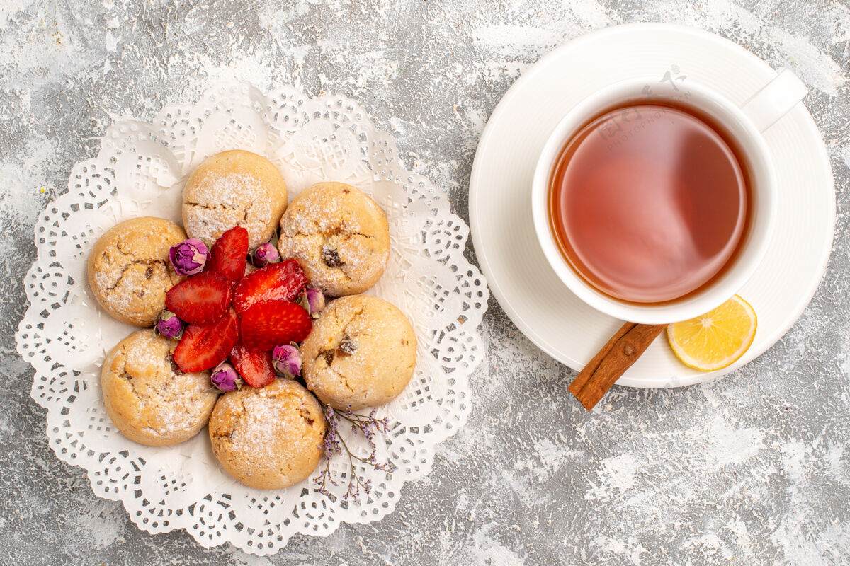 浆果在浅白色的表面上 可以看到美味的沙曲奇和新鲜的草莓以及一杯茶水果杯子茶