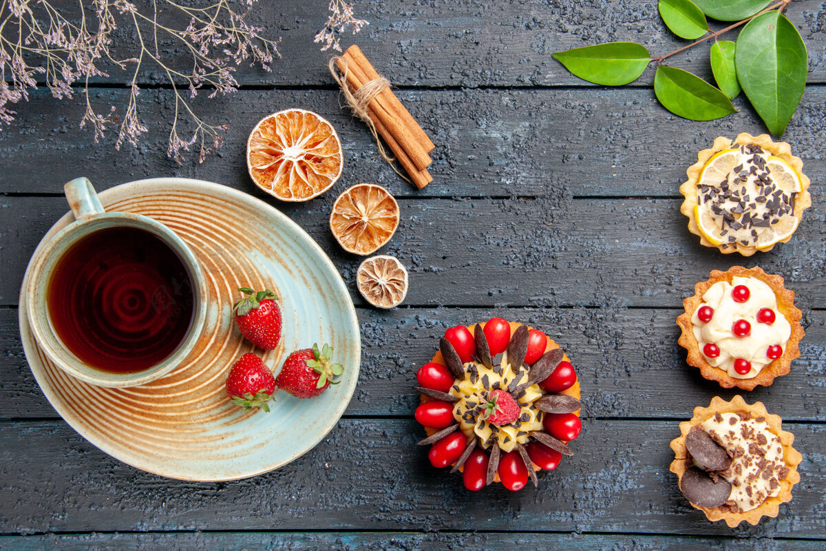 桌子顶视图一杯茶和草莓放在茶托上干橙子馅饼叶子和浆果蛋糕放在深色木桌上食物水果新鲜