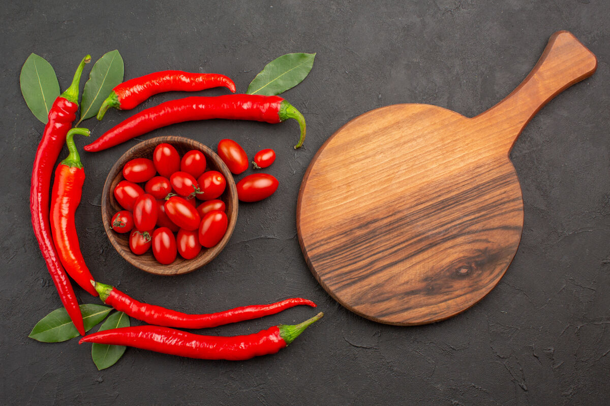 新鲜俯视图半圈红辣椒和月桂叶 一碗樱桃西红柿和一个椭圆形的砧板放在黑色的桌子上排骨烹饪食物