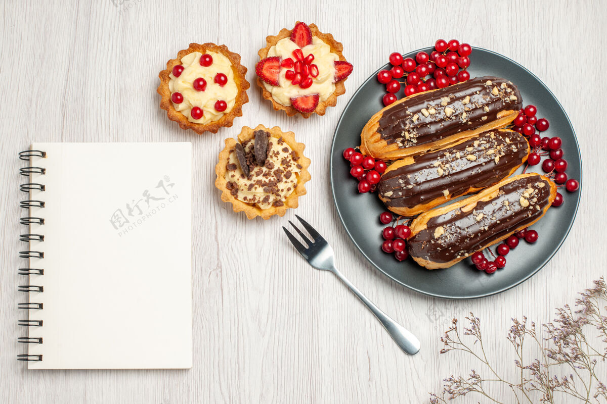 晚餐顶视图：灰色盘子上的巧克力蛋糕和葡萄干饼干 白色木桌上的叉子和笔记本头发滑木头桌子