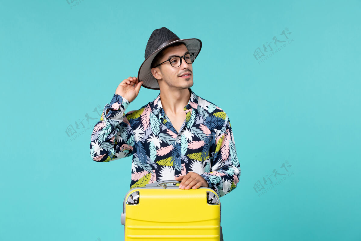 度假年轻男子正拿着他的黄色袋子准备在蓝色的墙上旅行旅行帽子肖像