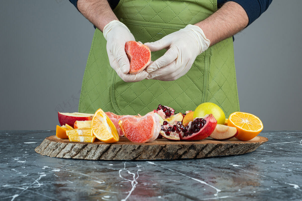 围裙男性手戴手套在大理石桌上切多汁的葡萄柚有机切片手套