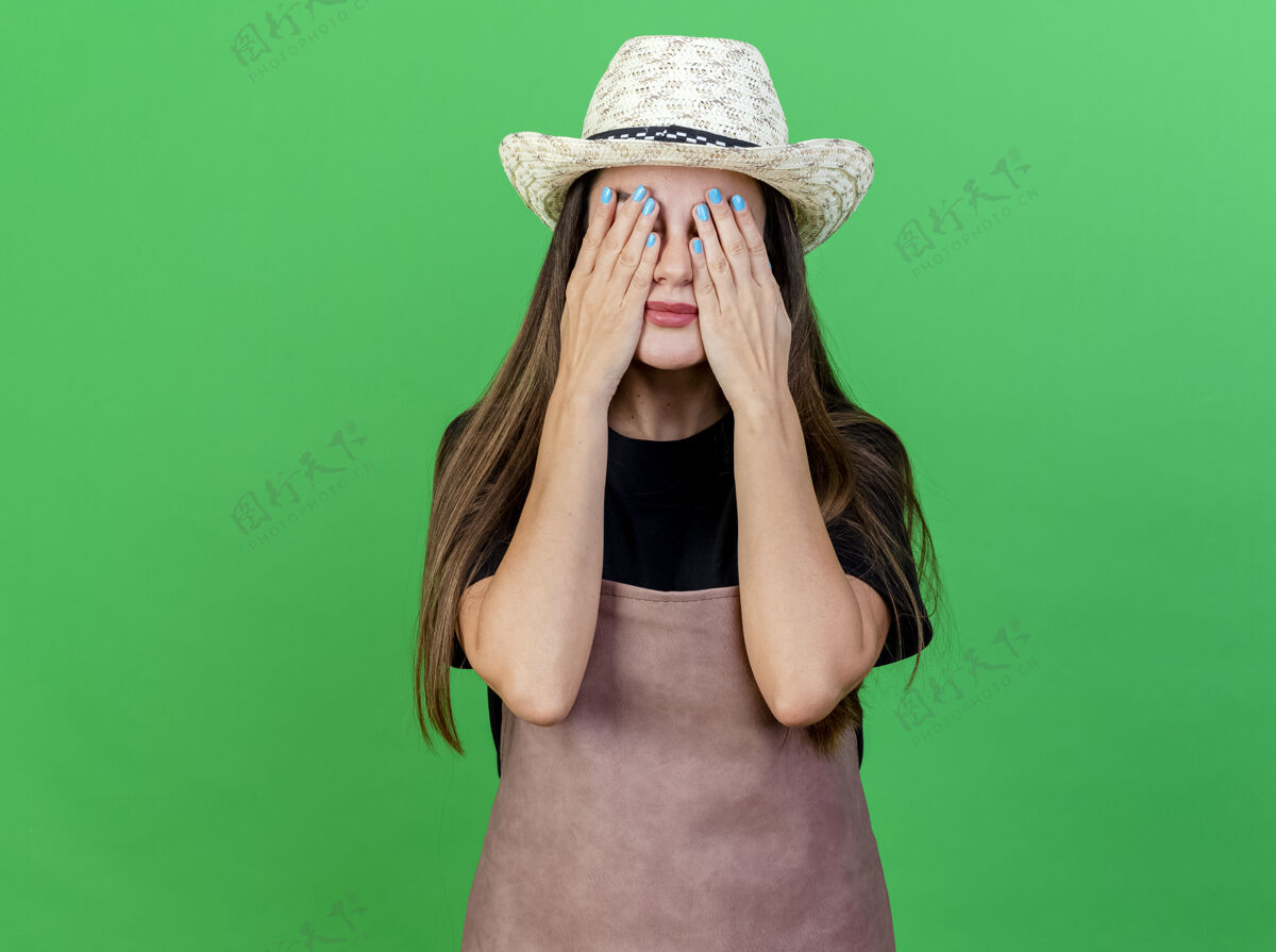 穿美丽的园丁女孩穿着制服戴着园艺帽双手眼睛孤立在绿色园艺花园眼睛