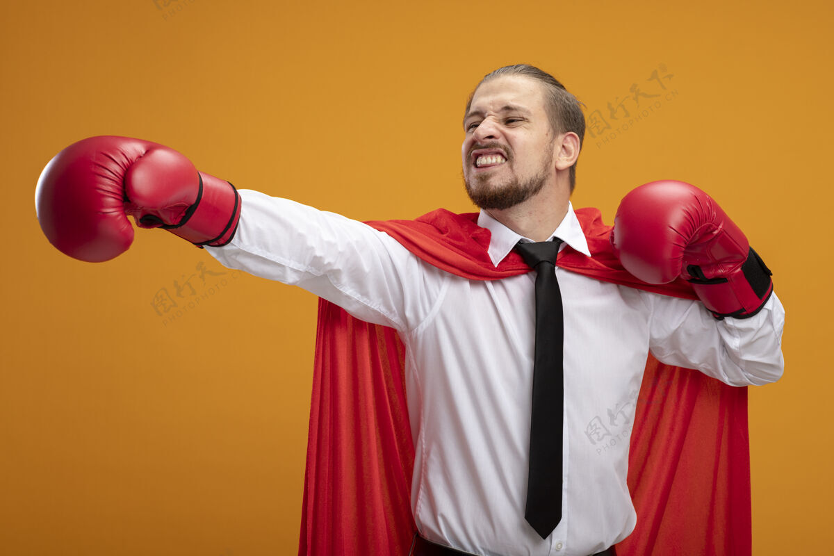 手套高兴的年轻超级英雄家伙戴着领带和拳击手套 伸出手在一边孤立的橙色请超级英雄举行