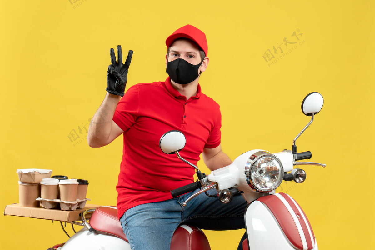 男人顶视图自信的年轻人穿着红色上衣 戴着帽子手套 戴着医用面罩 坐在踏板车上传递命令 黄色背景上有三个摩托车背景命令