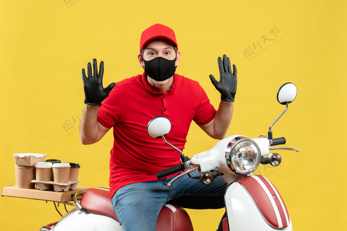 坐顶视图勤劳的年轻人穿着红色上衣 戴着帽子手套 戴着医用面罩 坐在黄色背景的踏板车上传递命令手套头盔人