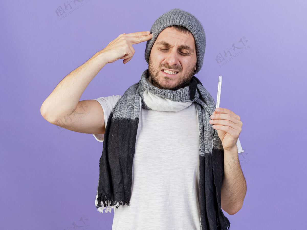太阳穴忧心忡忡的年轻病人戴着冬天的帽子 戴着围巾 拿着温度计 把手指放在紫色的太阳穴上戴着紫色年轻