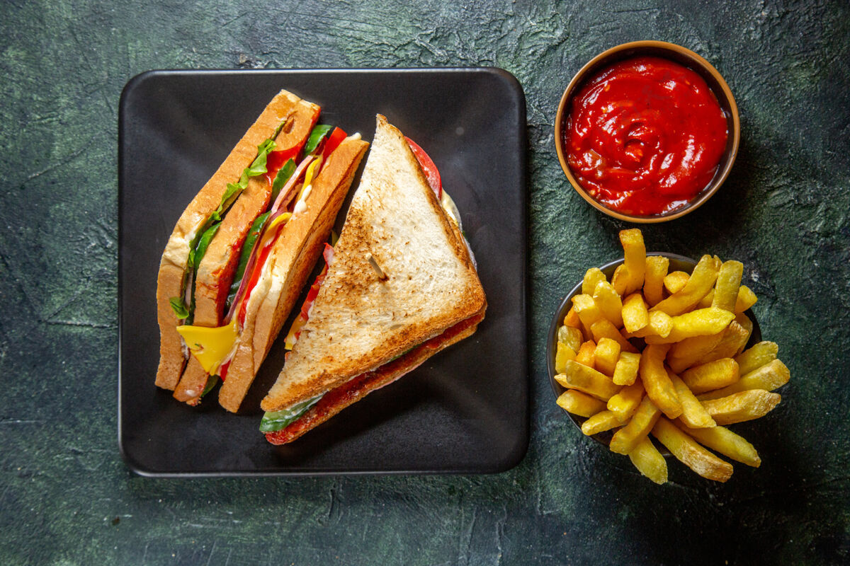 晚餐俯瞰美味的火腿三明治在黑暗的盘子里 炸薯条和番茄酱在黑暗的表面风景三明治食物