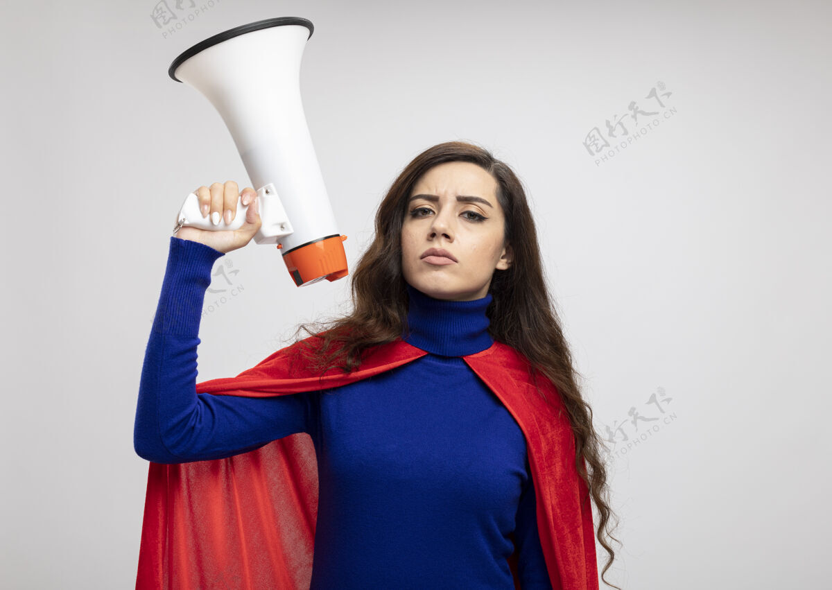 超级英雄自信的白种人超级英雄女孩 穿着红色斗篷 在白色墙壁上拿着一个独立的扩音器斗篷大声坚持