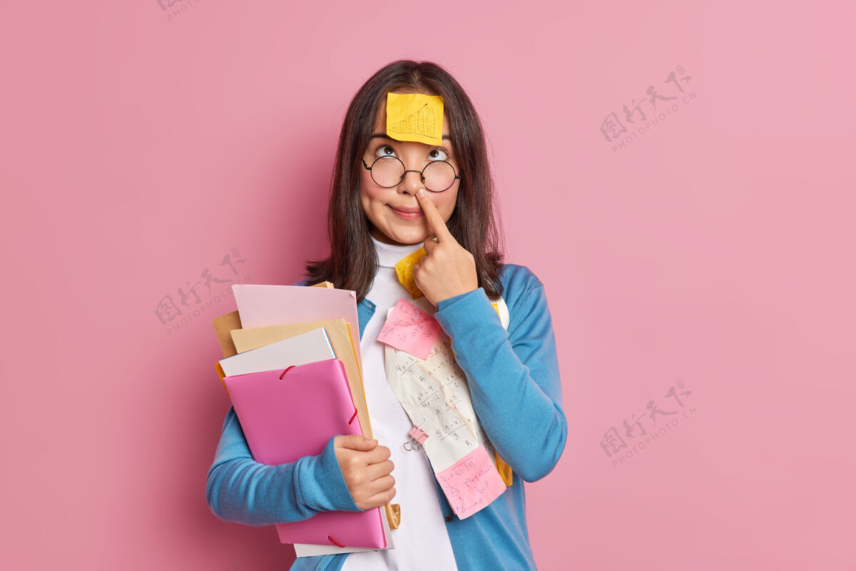 记住有趣的书呆子学生摸鼻子有贴在额头上的便签拿着文件夹和文件集中在上面为考试做准备女人在办公室用总数学习文件人毛衣女人