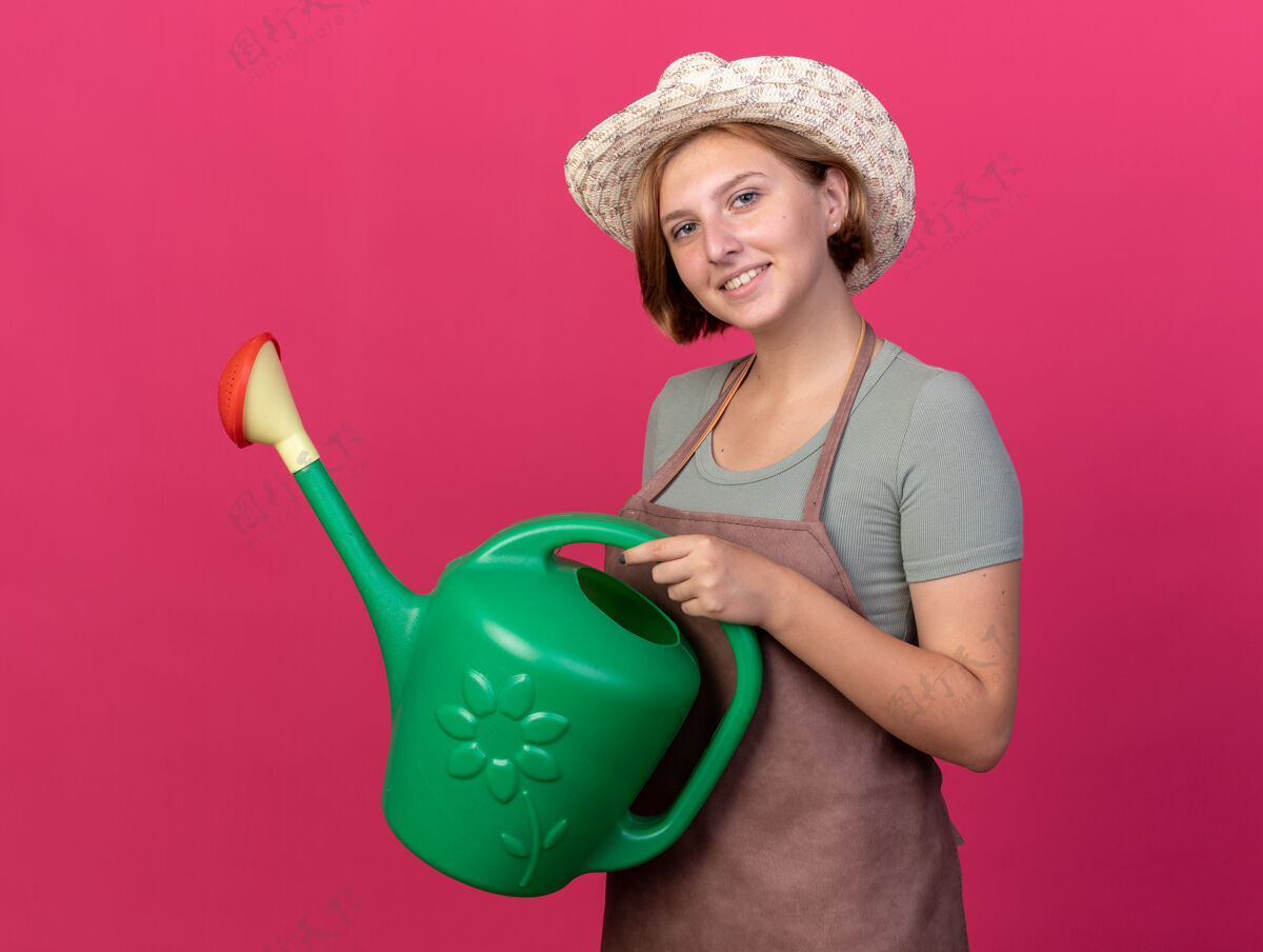 园艺微笑着的年轻斯拉夫女园丁戴着园艺帽拿着粉色的浇水罐年轻的女的浇水