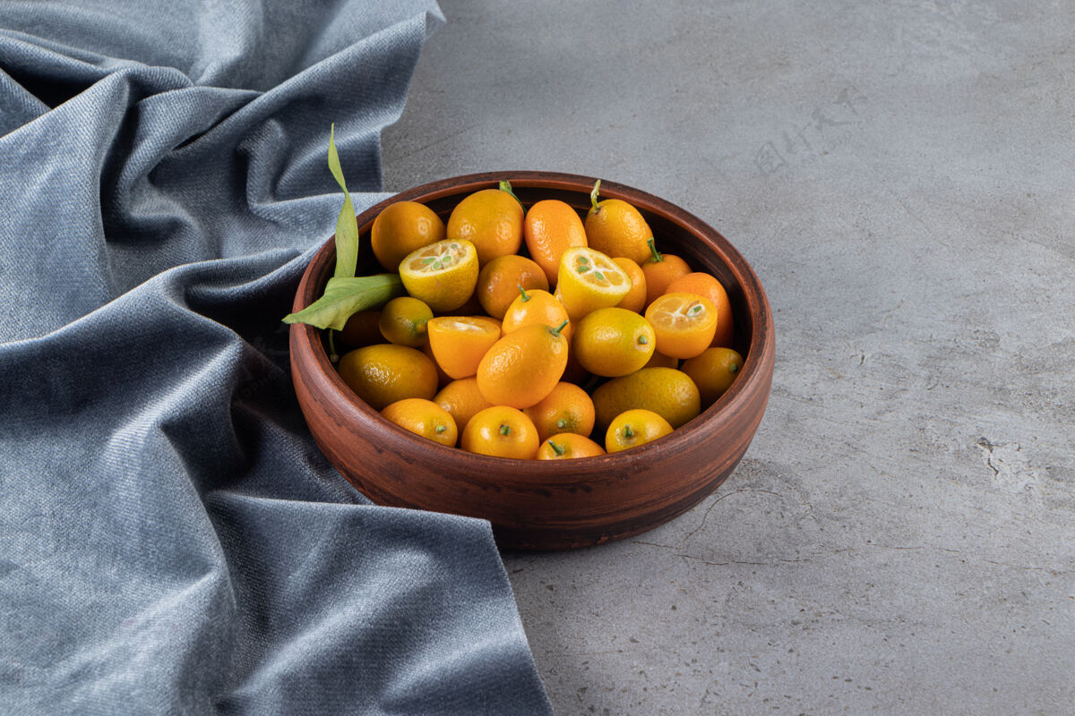 叶把金橘水果放在碗里的一块布上 放在大理石表面膳食配料丰盛