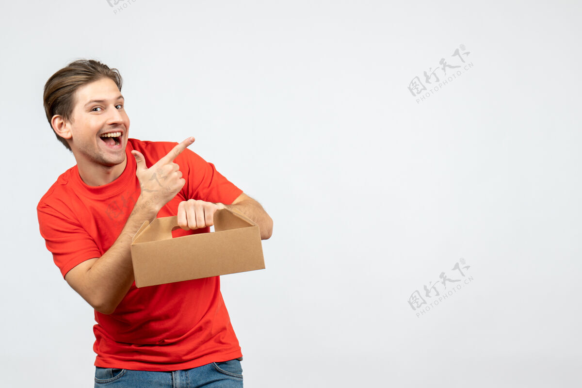 微笑俯视图：微笑着 情绪激动的年轻人 穿着红色上衣 拿着盒子 指着白墙上左边的东西左边壁板抱着