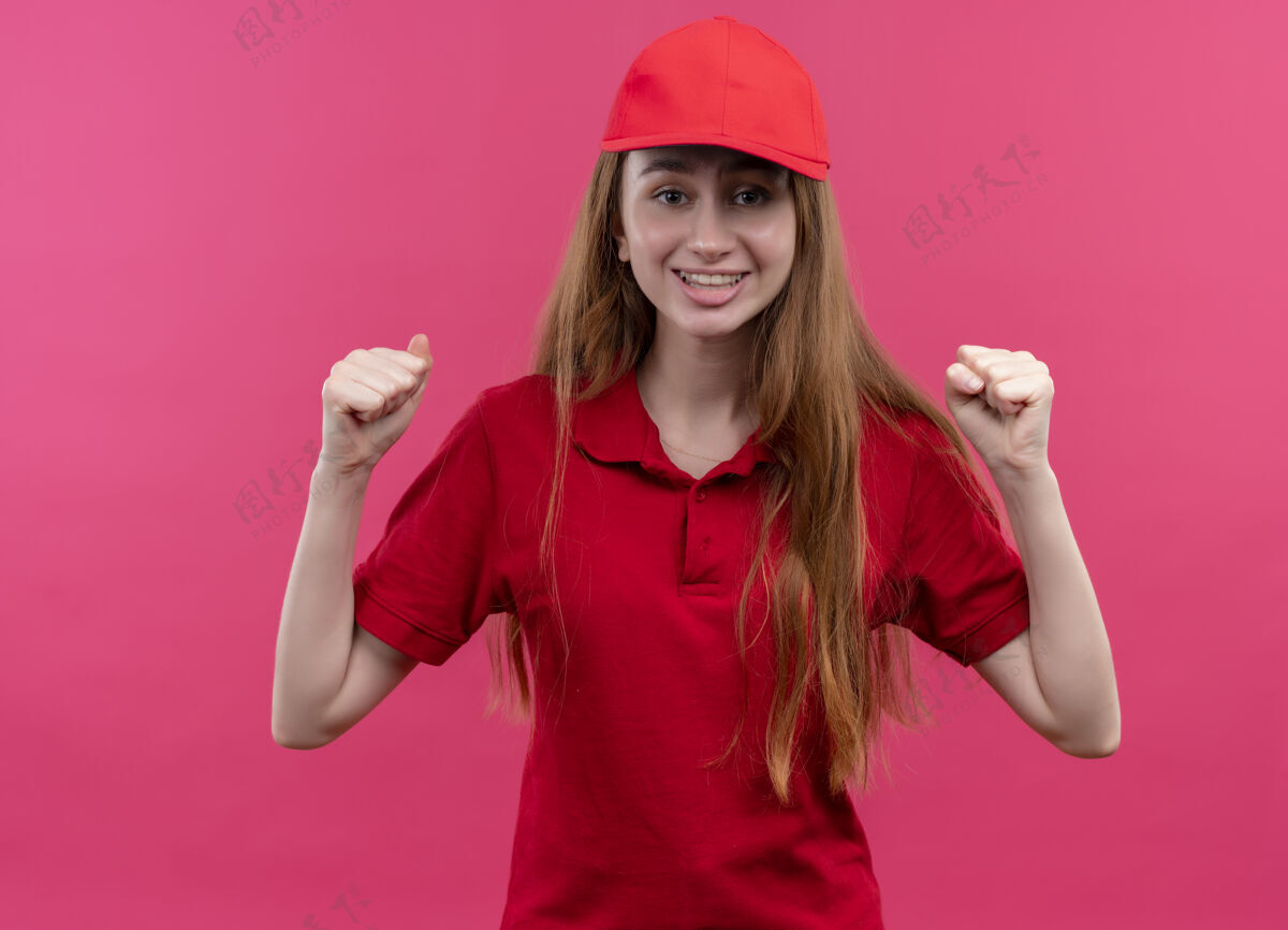 女孩快乐的年轻送货女孩穿着红色制服 在孤立的粉红色空间举起拳头提高交付红色