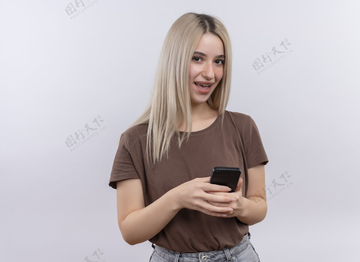 年轻快乐的年轻金发女孩戴着牙套拿着手机在隔离的空白处与复印空间复制女孩手机