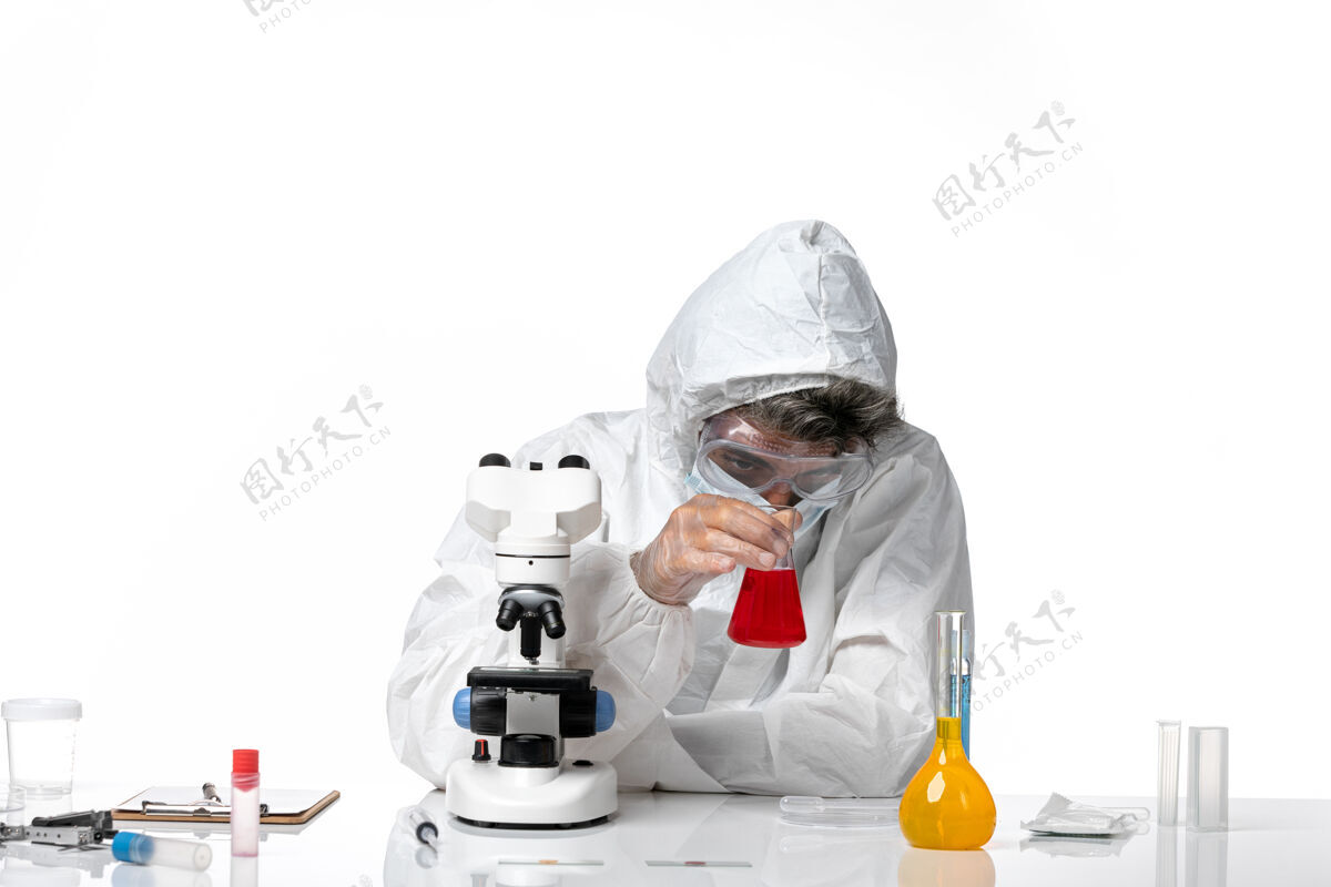 套装正面图：男医生穿着防护服 戴着口罩 白色桌子上拿着装有红色溶液的瓶子 大流行性冠状病毒健康病毒专业人男医生