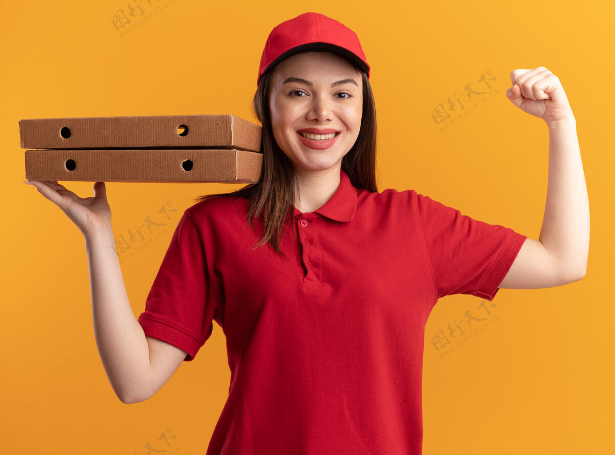 微笑微笑的漂亮送货员穿着统一的时态二头肌 拿着放在橘子上的披萨盒女人制服橘子