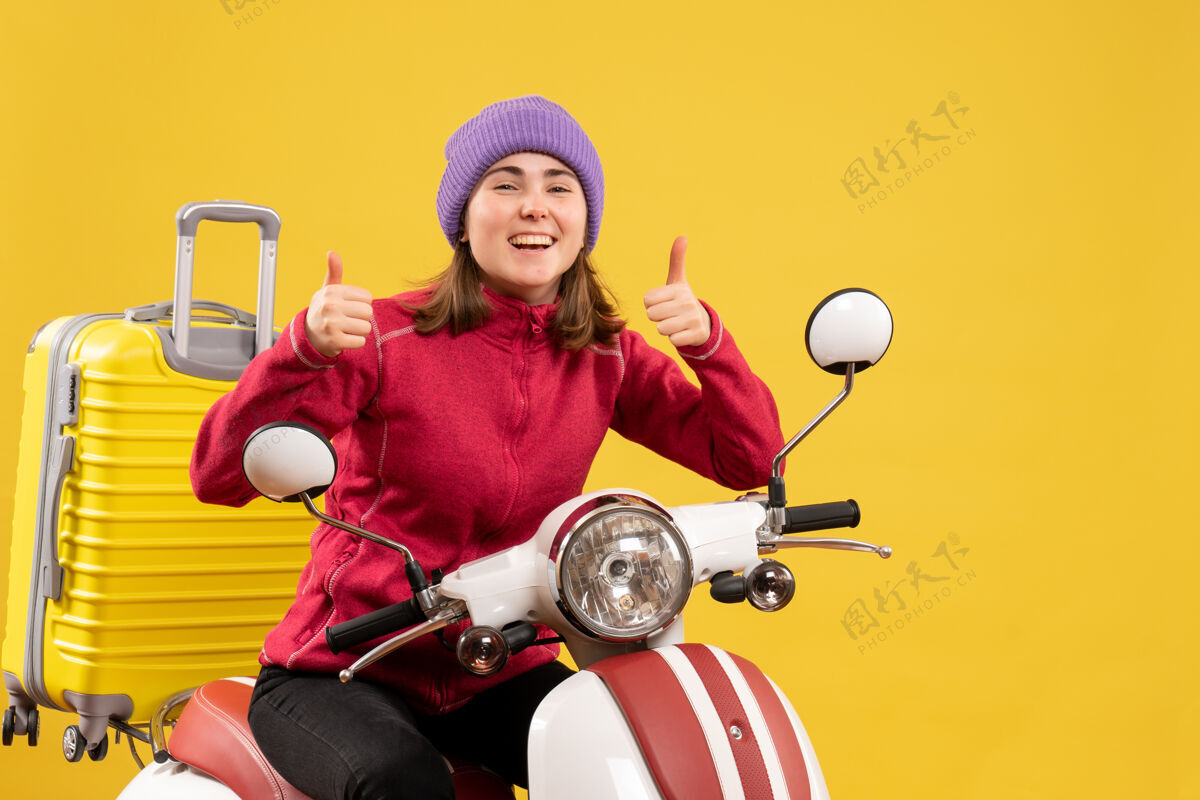 轻便摩托车正面图：骑着轻便摩托车的年轻女子兴高采烈地竖起大拇指给予微笑坐