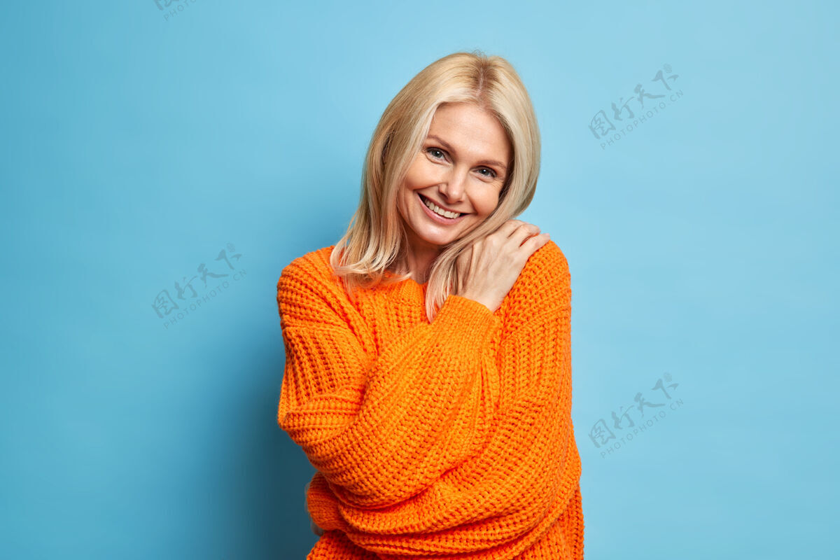 乐观美丽微笑的金发女人抱着自己看起来温柔满足的表情歪着头穿着暖和的针织毛衣高兴魅力皱纹