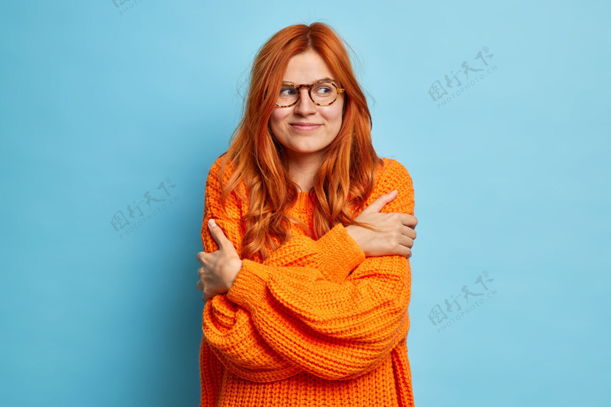 站着漂亮的红发女子拥抱自己喜欢她的新针织橙色毛衣看起来满意的权利舒适毛衣橙色