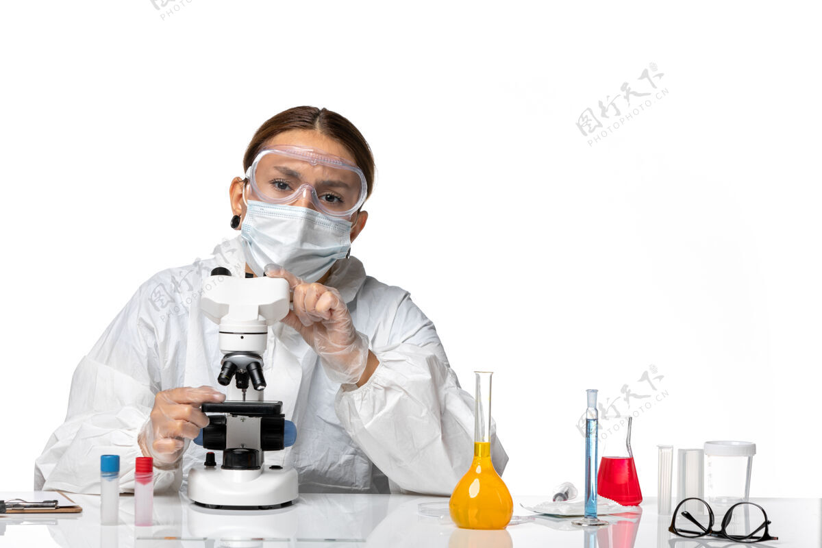 流行前视女医生穿着特制的工作服 戴着口罩 用显微镜观察白色背景的冠状病毒大流行外套医生女医生