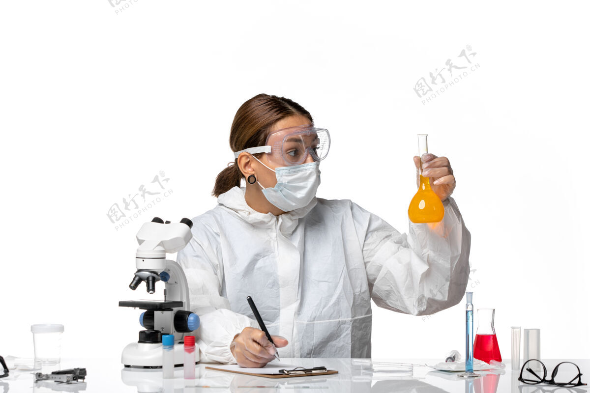 外套正面图：女医生 穿着特制的工作服 戴着口罩 拿着装有黄色溶液的烧瓶 在白色背景上写着大流行冠状病毒实验室外套保持女医生