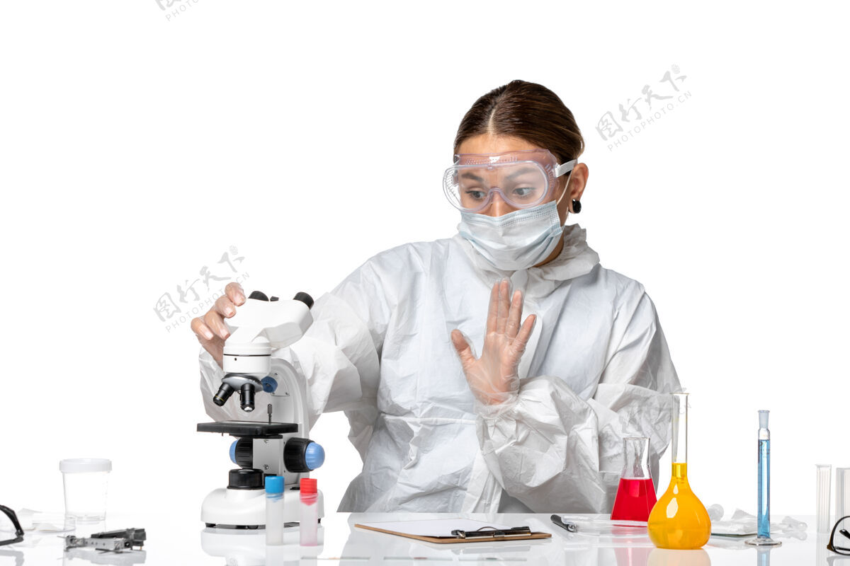 医疗正面图女医生穿着防护服 戴着口罩用显微镜在白色背景上观察健康冠状病毒大流行视图使用外套