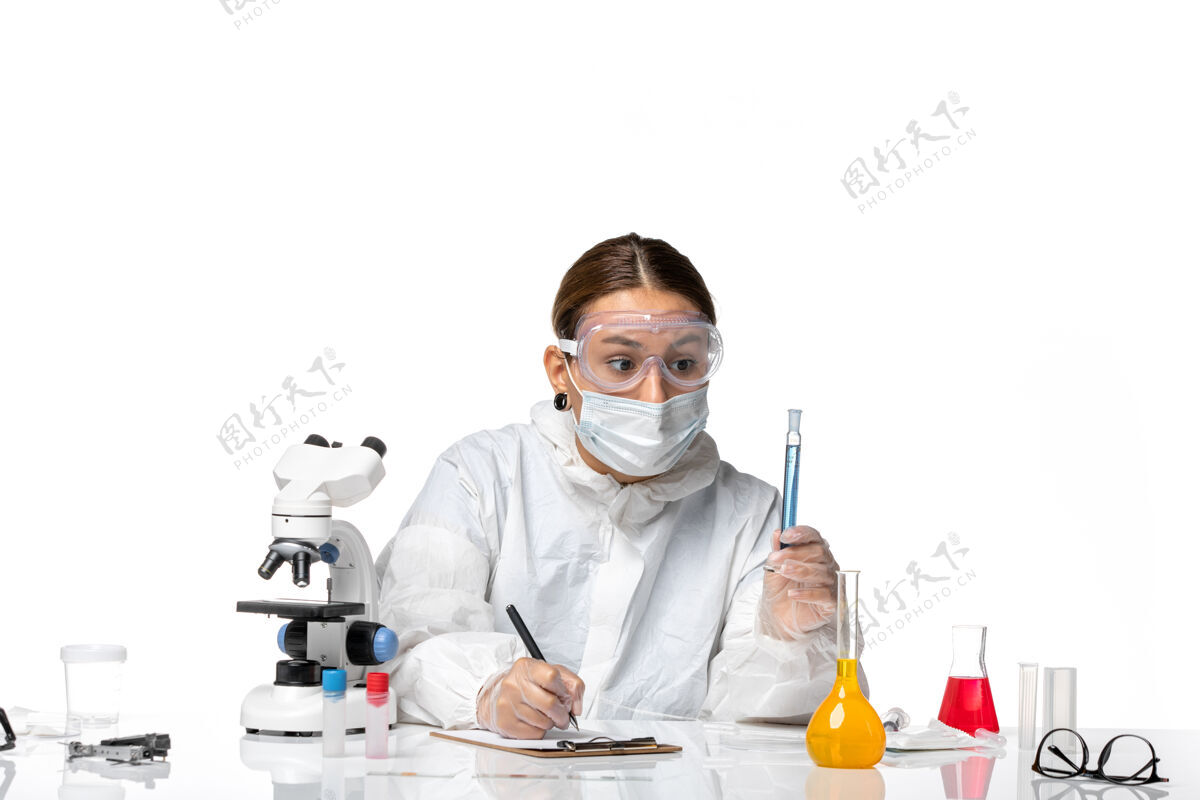 视图正面图：女医生穿着防护服 戴着面罩 上面拿着蓝色溶液 写着白色背景的冠状病毒大流行病毒的笔记持有防护专业