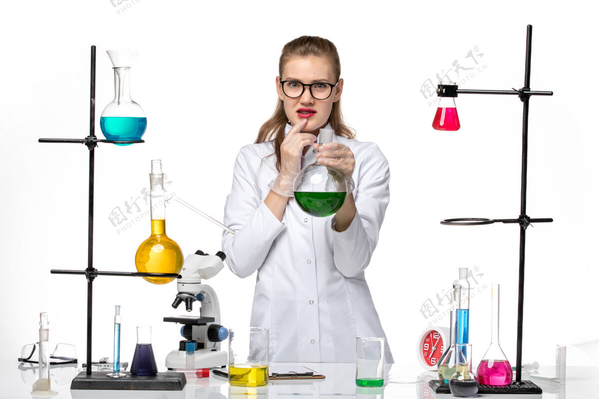 医学前视图穿着医疗服的女化学家拿着一个装有绿色溶液的烧瓶 背景是白色的化学大流行性冠状病毒绿色视野专业