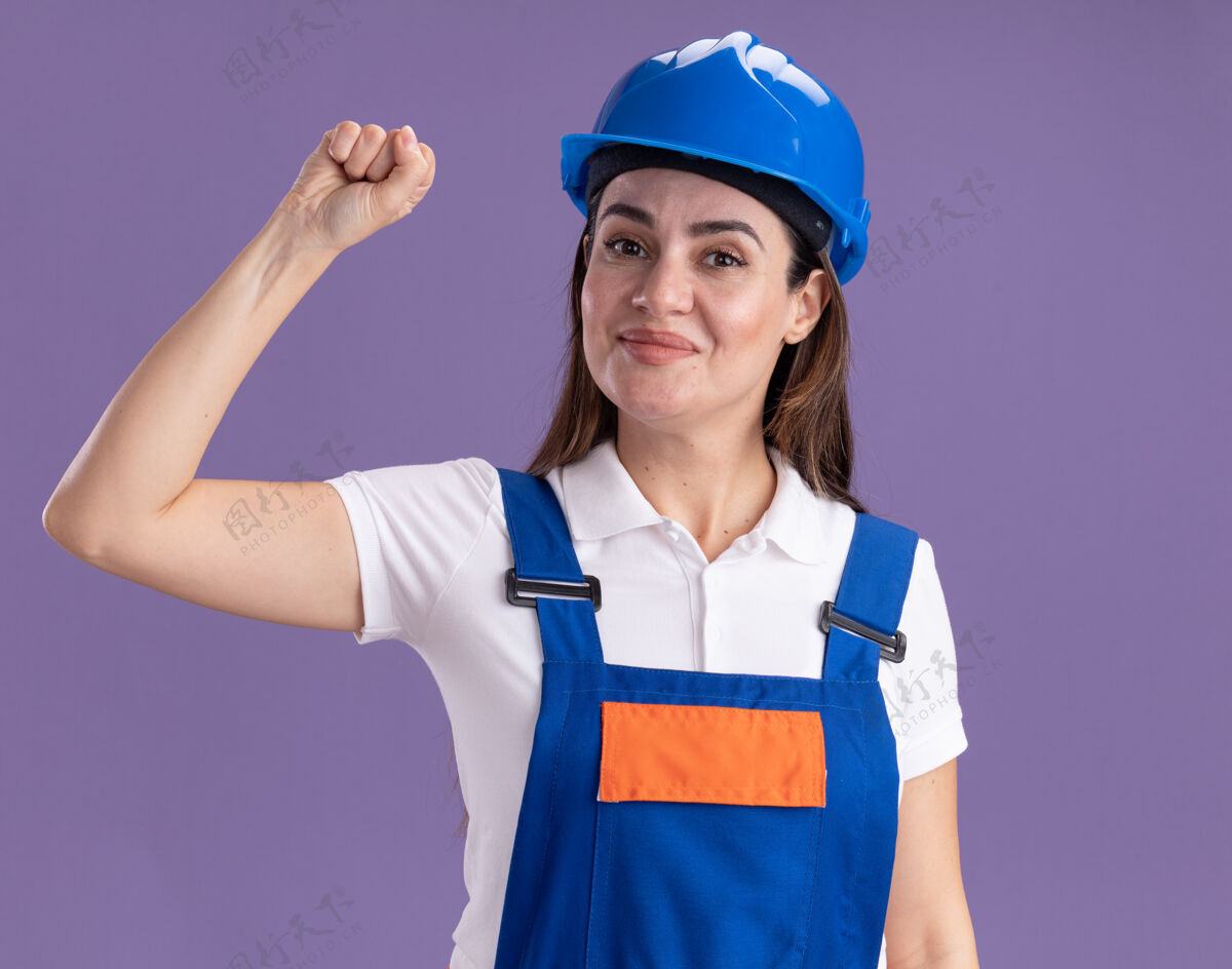 请身着制服的年轻建筑工人高兴地在紫色的墙上显示“是”的手势衣服制服表演
