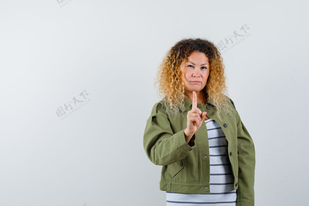 金发漂亮的金发女人穿着绿色夹克用食指警告 看起来很严肃 正面视图手指毛衣肖像