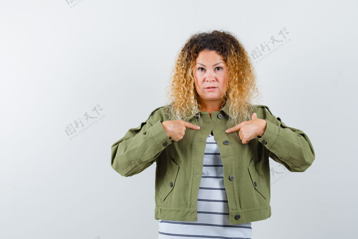 退休一个女人的肖像 卷曲的金发指着穿着绿色夹克的自己 看着困惑的前视图成熟时尚老年人