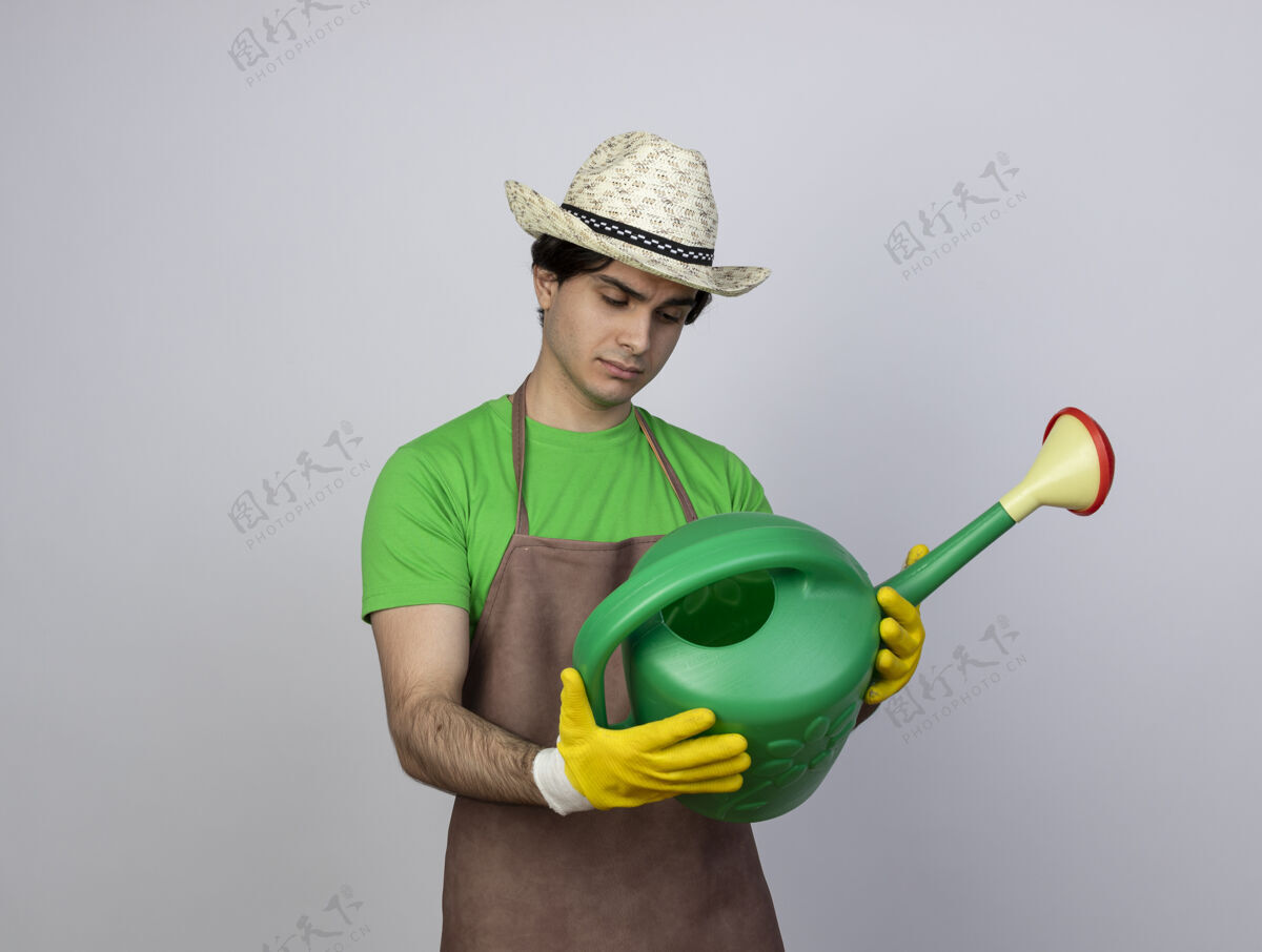 男人想着穿着制服的年轻男园丁戴着园艺帽和手套拿着浇水罐看着浇水人园艺
