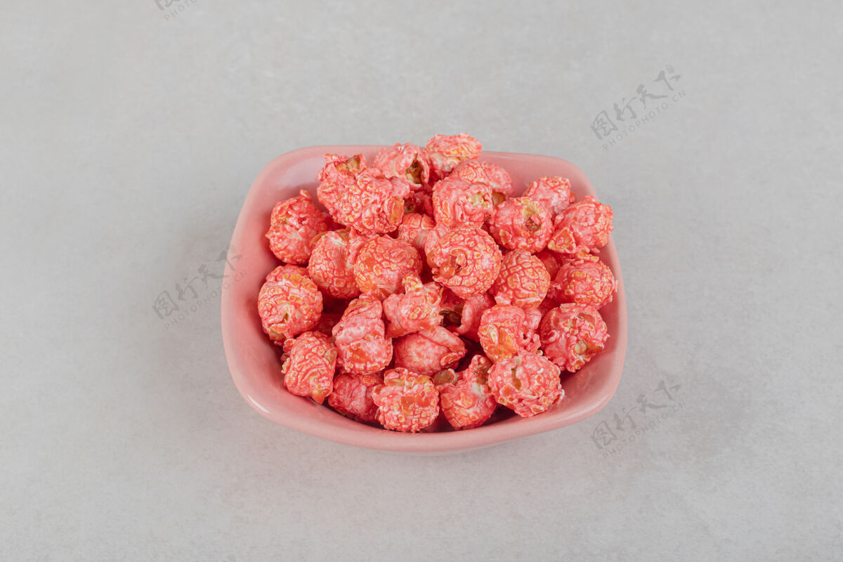 碗放在大理石桌上粉红色盘子上的一小堆有香味的爆米花垃圾食品外套不健康