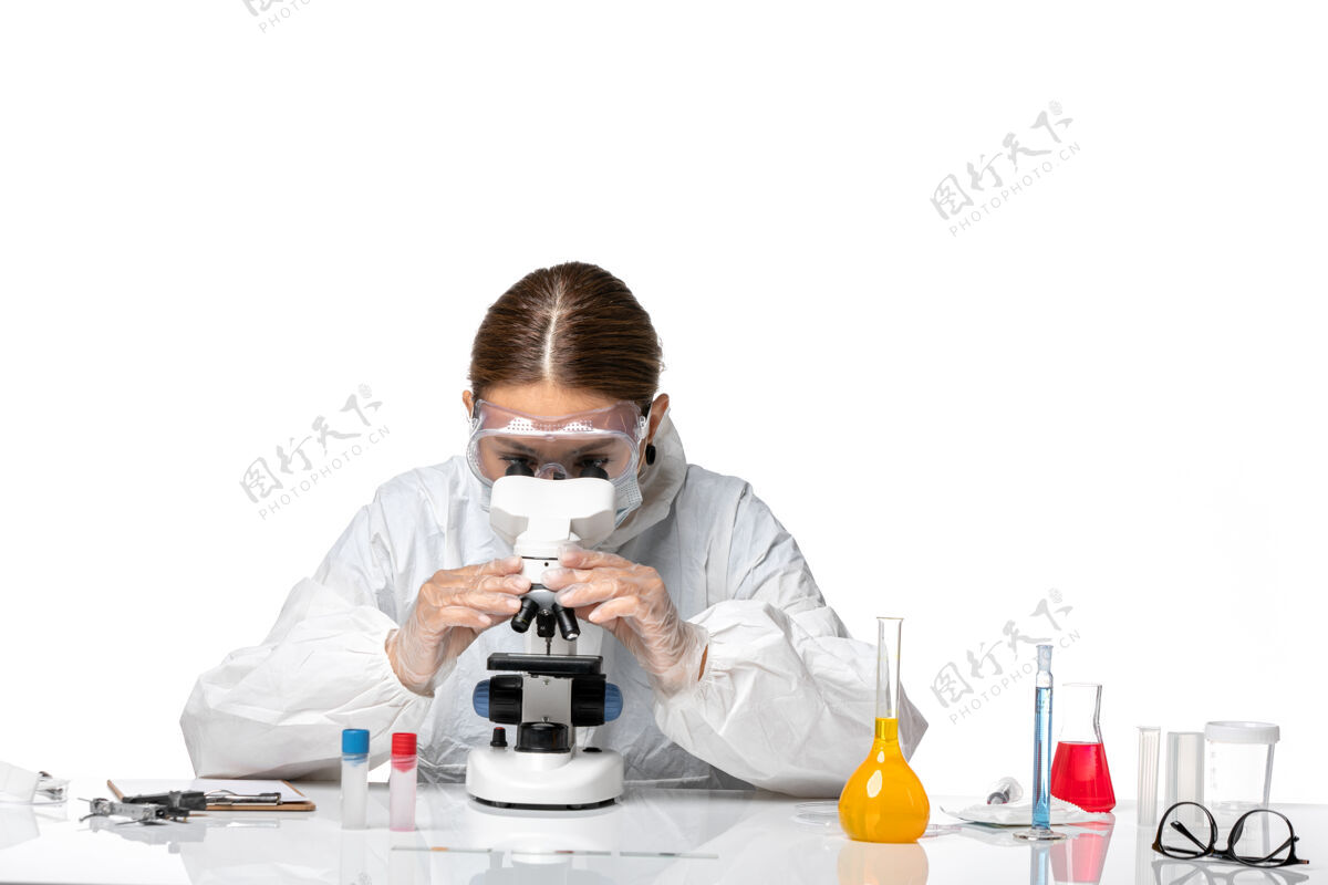 医疗正面图女医生穿着特制的工作服 戴着口罩 用显微镜观察一种白色背景的冠状病毒大流行套装口罩人