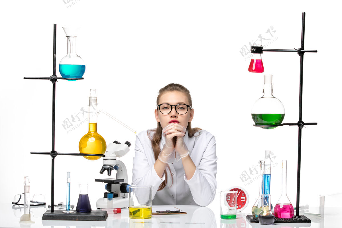 专业前视图穿着白色医疗服的女医生坐在桌子前 拿着白色背景的化学病毒大流行的解决方案坐男人桌子