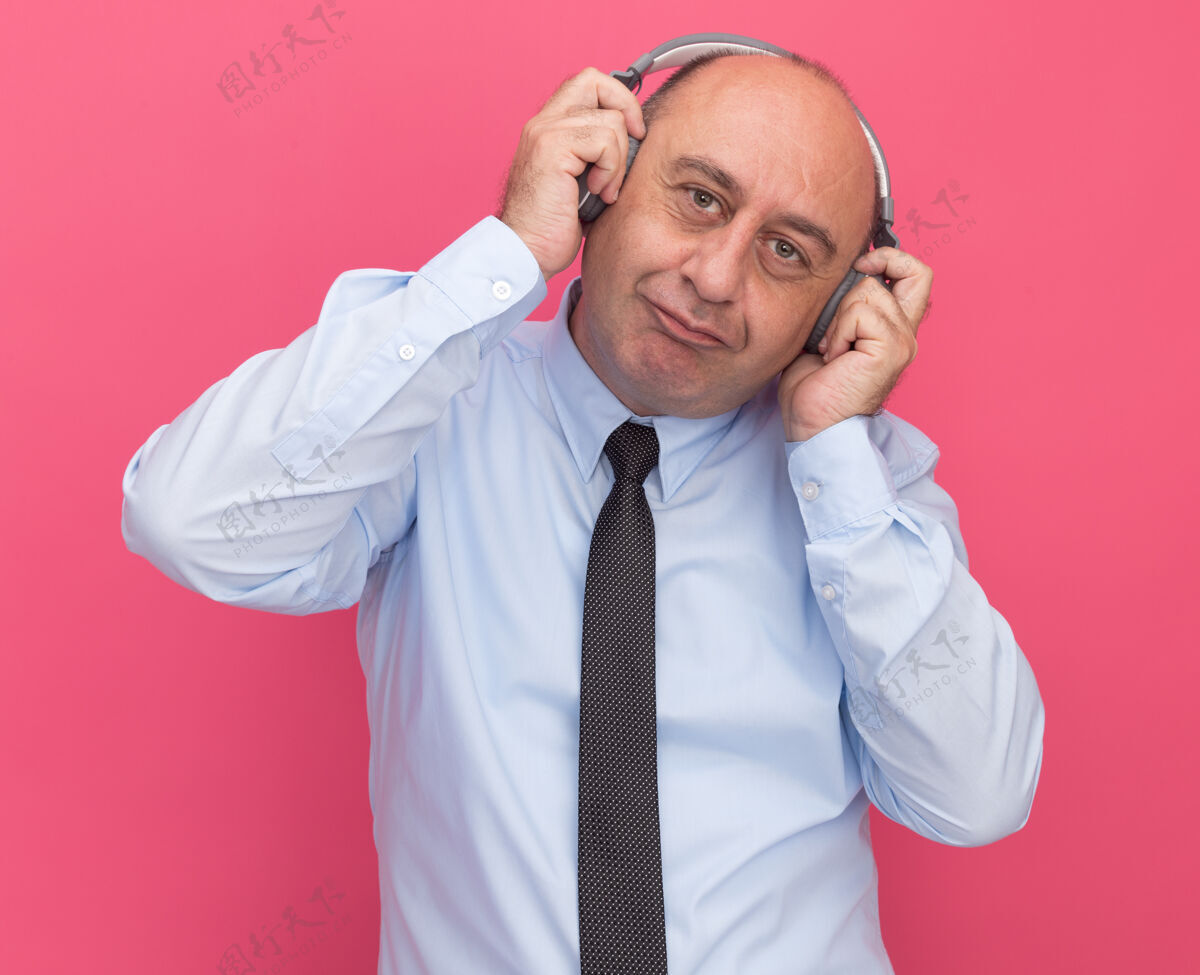 公民喜欢歪着头的中年男子穿着白色t恤 打着领带 把耳机孤立在粉红色的墙上姿势表情领带